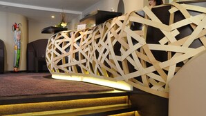 A reception desk with a wooden lattice design, a purple carpeted area, and a staircase with wooden steps. - Hotel Freund (Voehl)