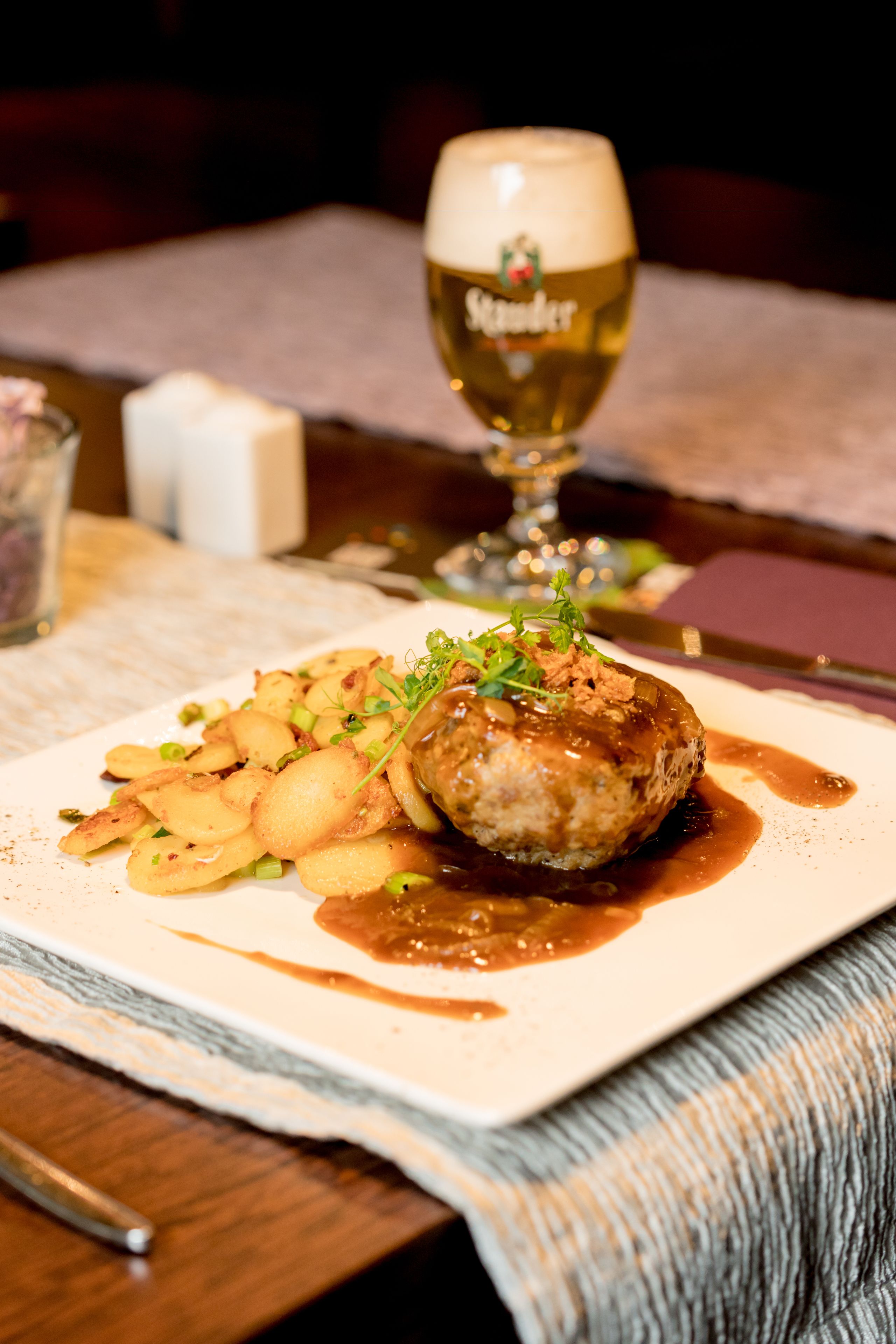 Un plato de comida con una hamburguesa, papas y salsa, acompañado de una cerveza.