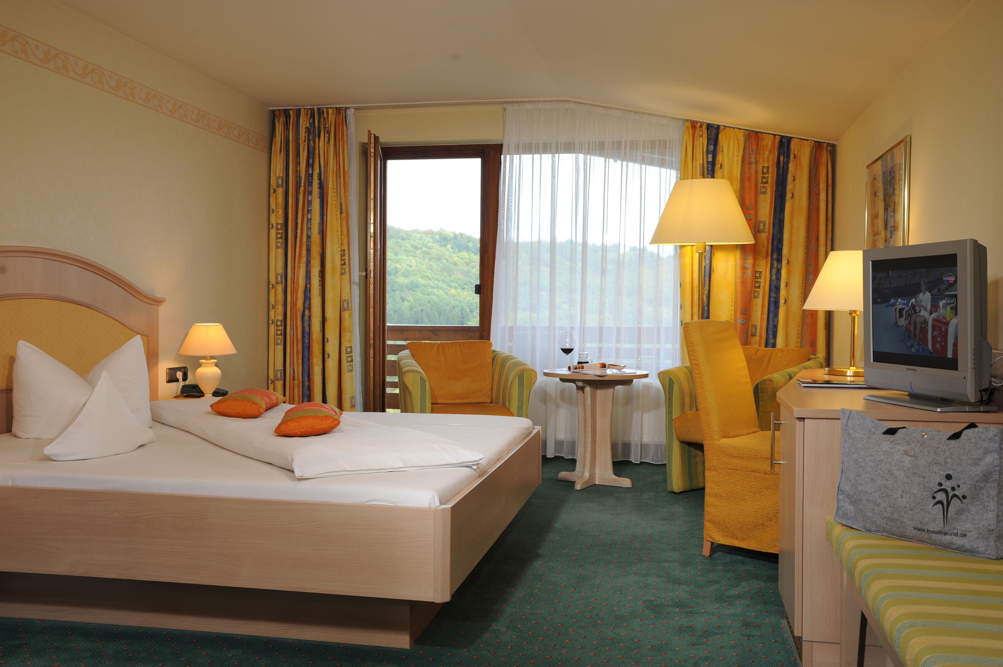 A hotel room with a bed, two chairs, a small table, a television, and a window with curtains.