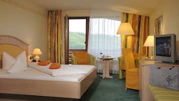 A hotel room with a bed, two chairs, a small table, a television, and a window with curtains.