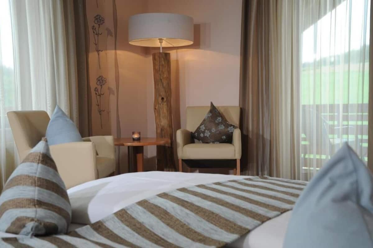 Habitación de hotel con una cama, dos sillas, una mesa, una lámpara y vistas a un campo verde a través de la ventana.