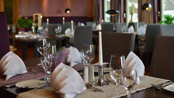 Een gedekte eettafel met witte servetten, wijnglazen en een brandende kaars, wat wijst op een formele setting in een restaurant.