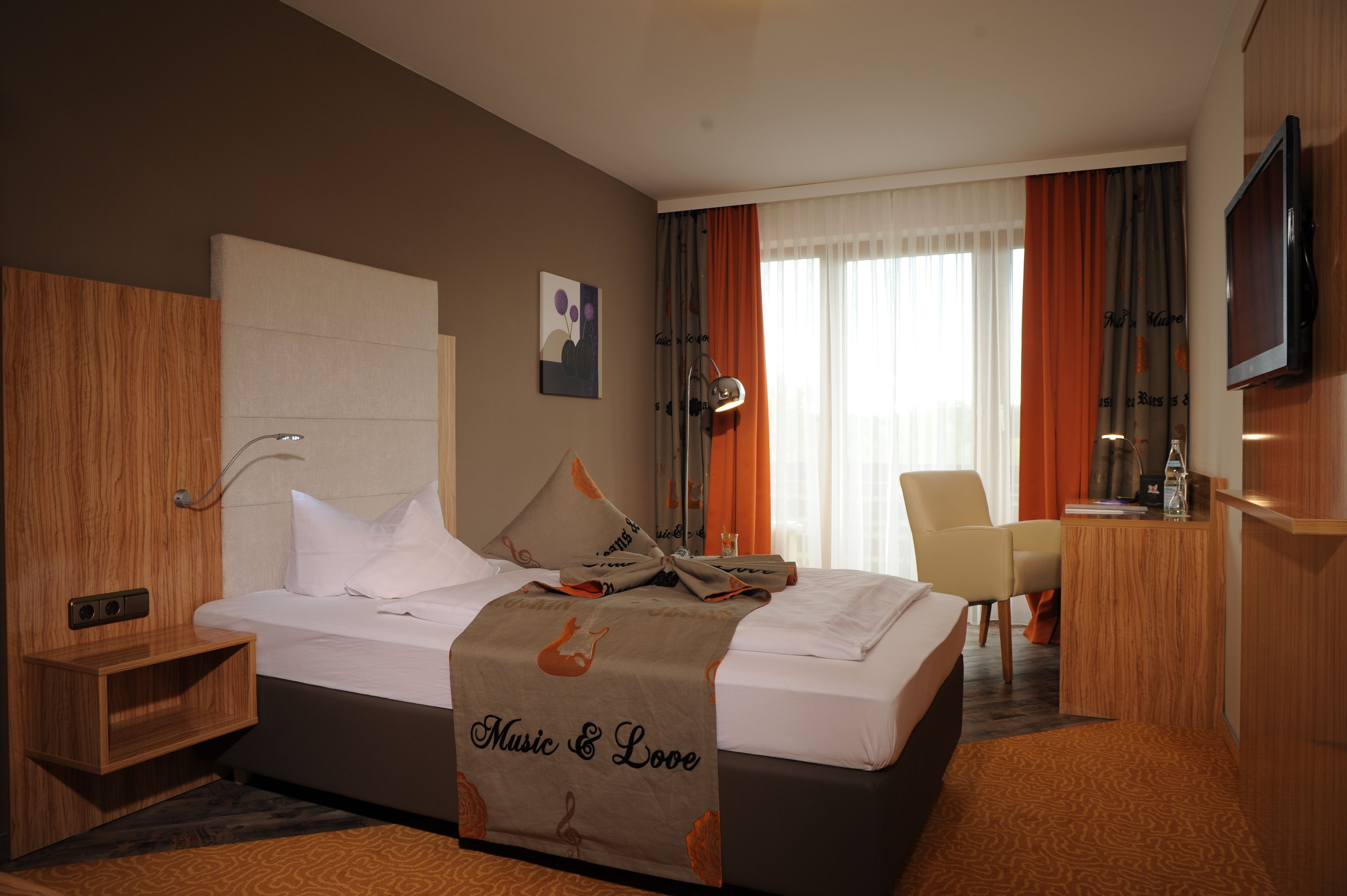 A hotel room with a bed, a desk, a chair, a TV, and a window with curtains.