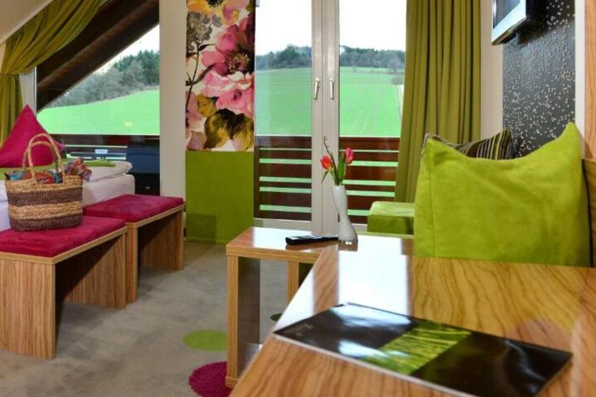Habitación de hotel moderna con una cama, una mesa de madera, un pequeño sofá y vistas a un campo verde.