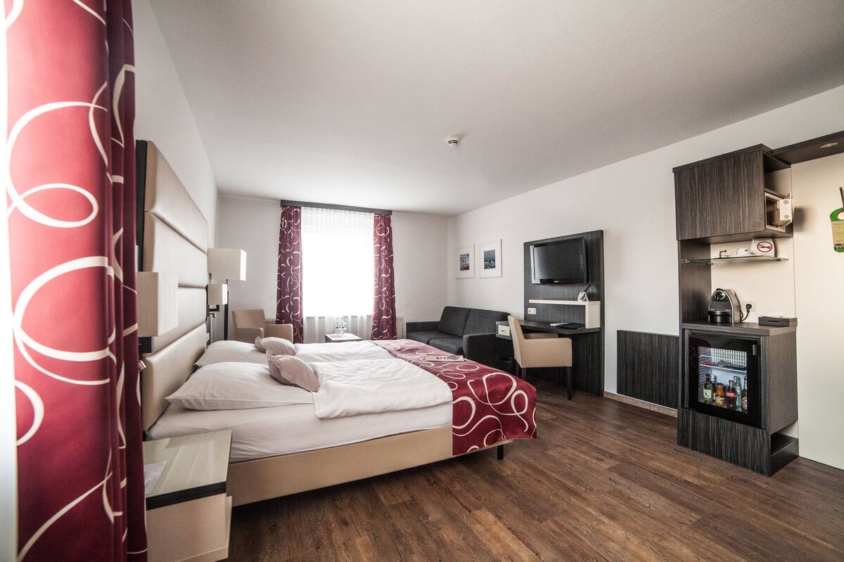 A hotel room with a bed, desk, chair, and a minibar.