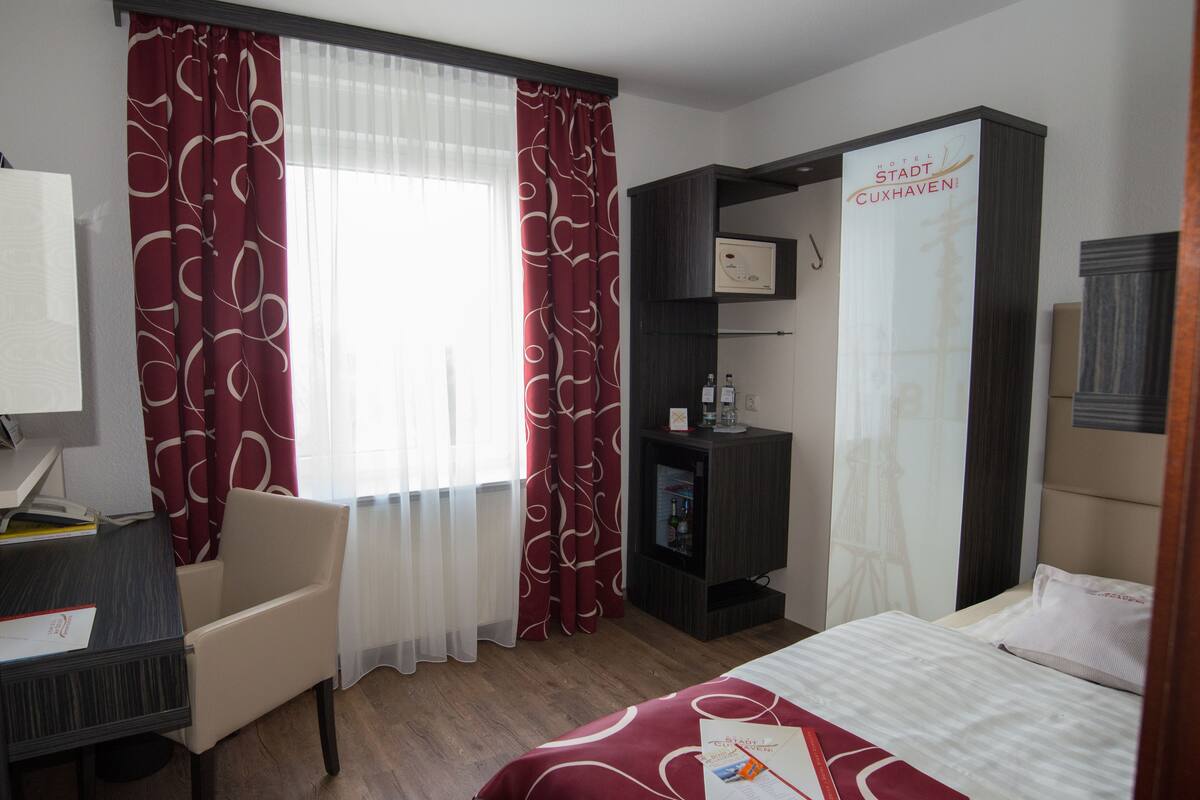 A hotel room with a bed, a desk, a chair, a TV, and a minibar.