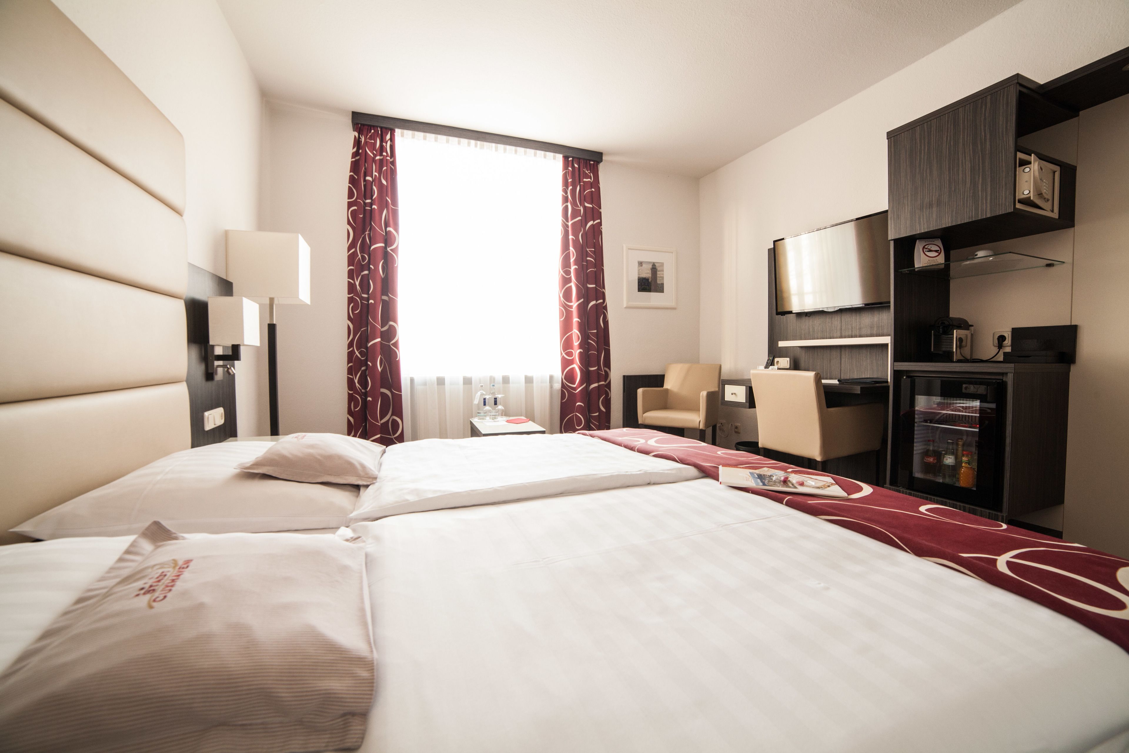 A hotel room with two beds, a desk, a chair, a minibar, and a television.