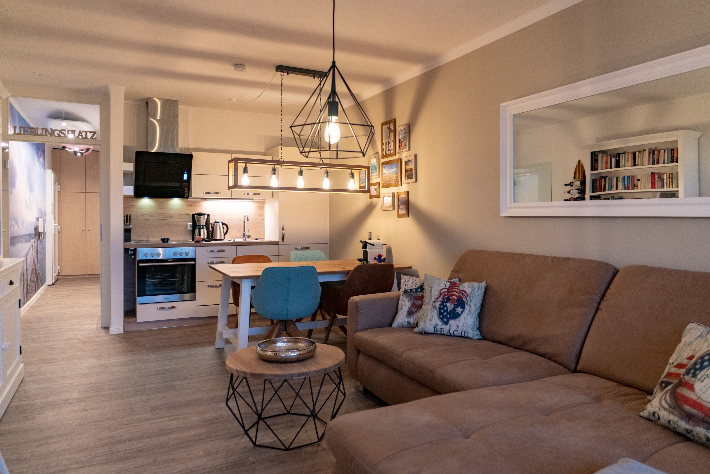 A modern kitchen with a dining area, a sofa with decorative pillows, and a bookshelf.