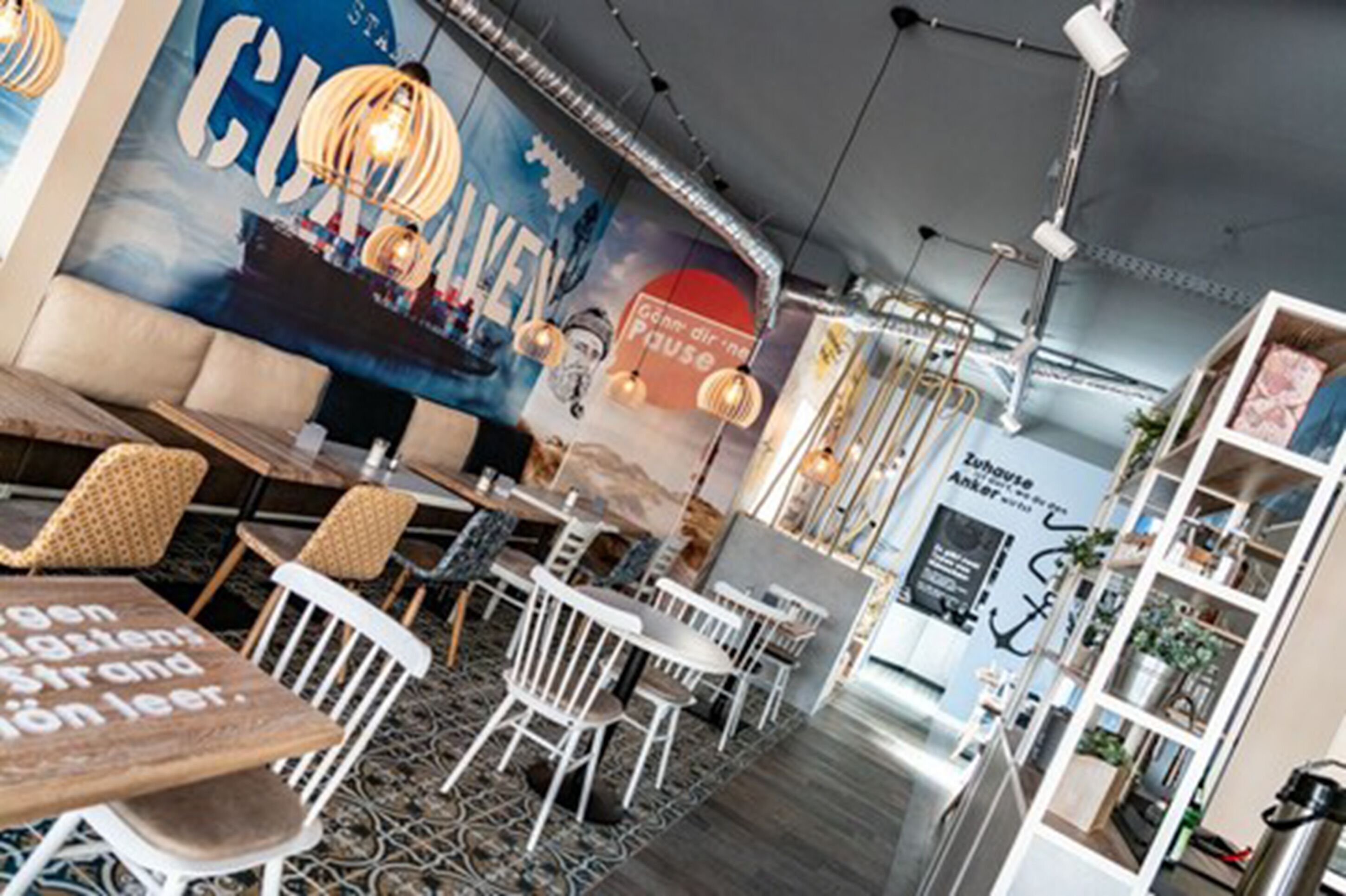 Un interior de restaurante moderno con mesas y sillas, iluminación decorativa y un mural en la pared.