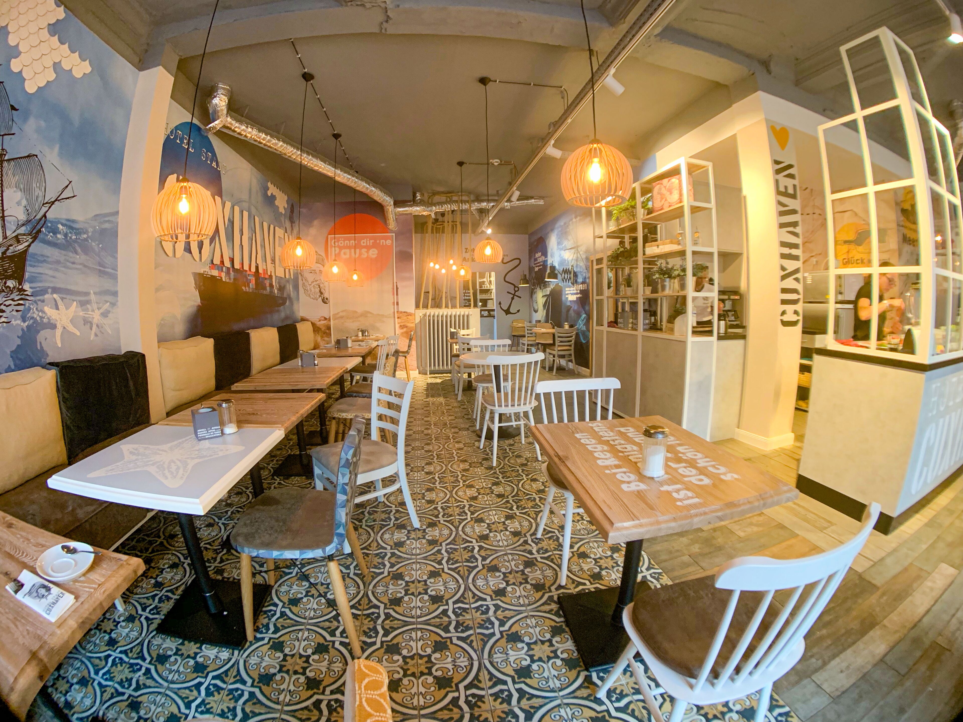 A restaurant with booths and tables, patterned floor tiles, and hanging pendant lights.