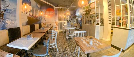 A restaurant with booths and tables, patterned floor tiles, and hanging pendant lights.