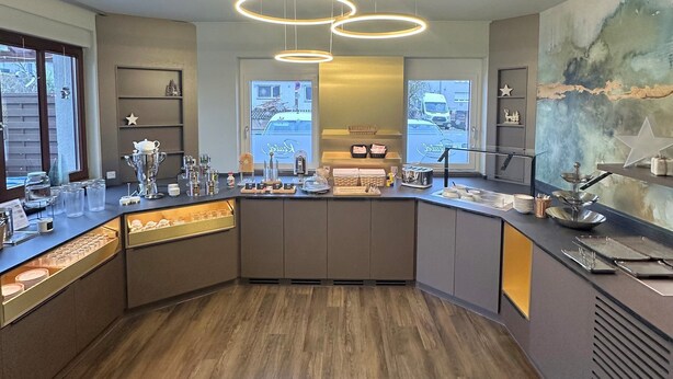 Una cocina moderna con una isla curva, iluminación colgante y vistas a la calle a través de amplios ventanales.