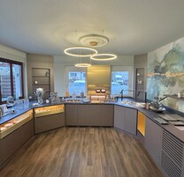 A modern kitchen with a curved island, pendant lighting, and a view of the street through large windows.