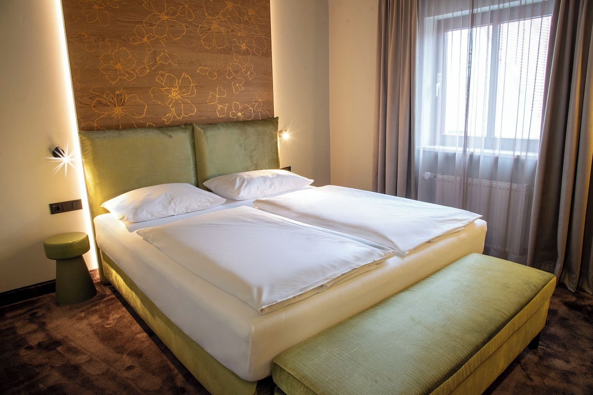 A hotel room with a bed, a bedside table, and a window with curtains.