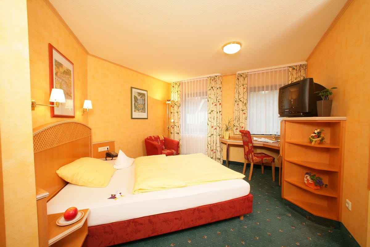 A hotel room with a bed, a desk, a chair, a television, and a shelf with decorative items.