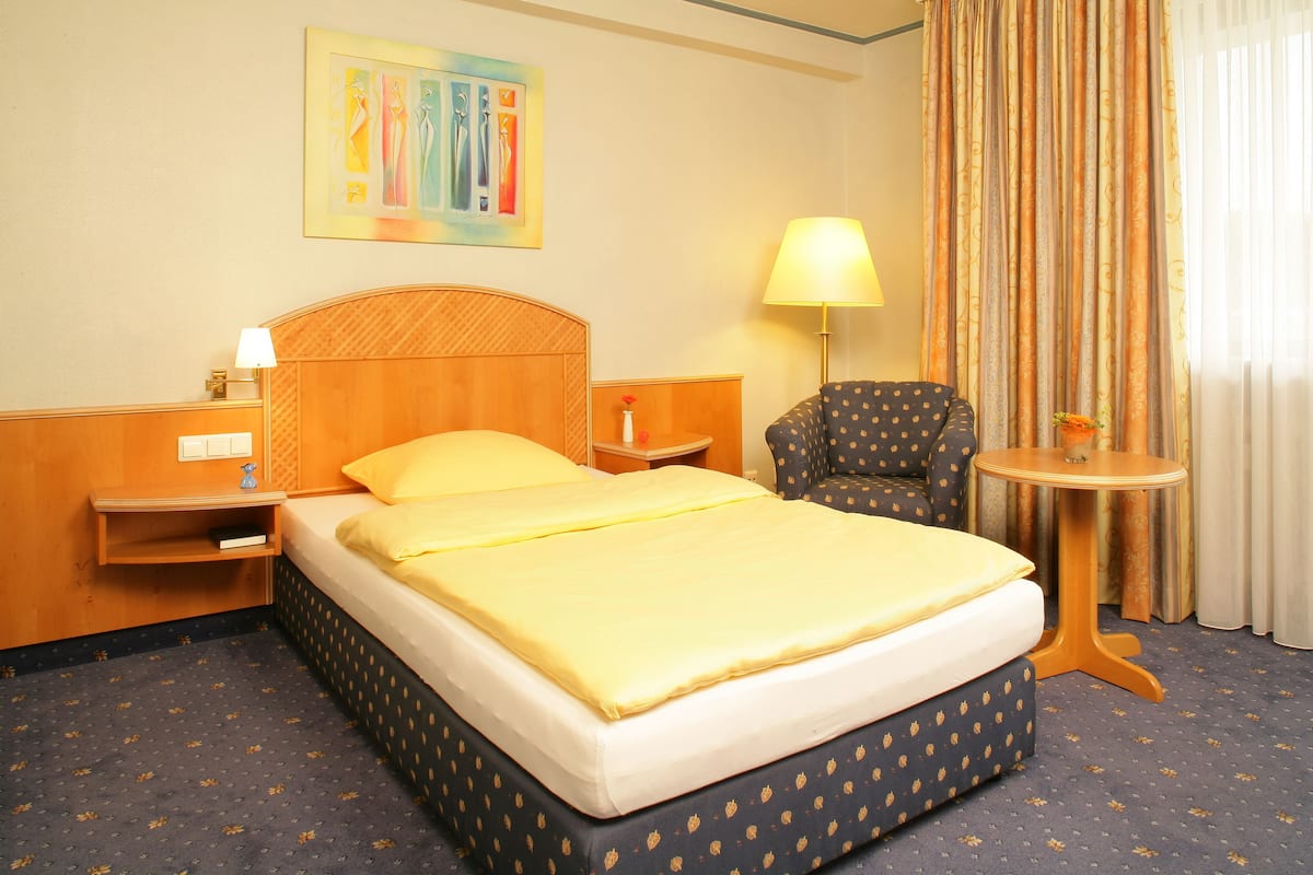 A hotel room with a bed, a chair, a small table, and a lamp.