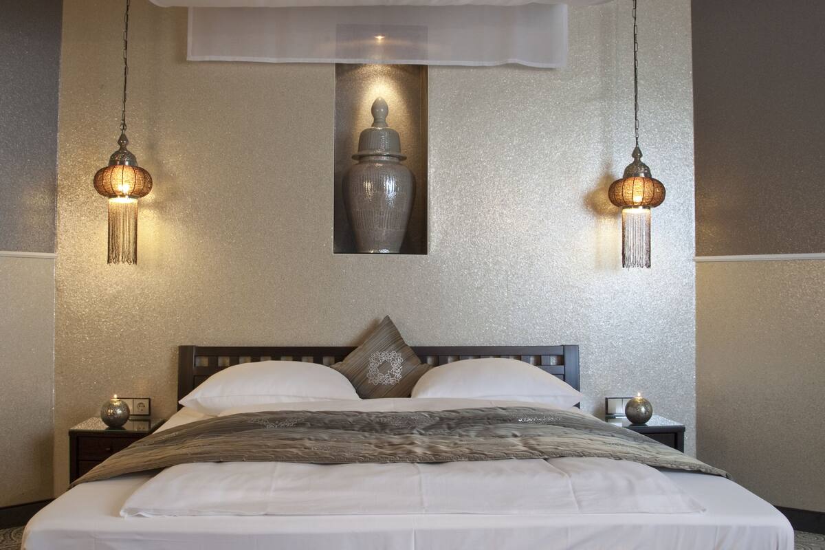 A neatly made bed with a white bedspread, two bedside lamps, and a decorative vase on the wall.