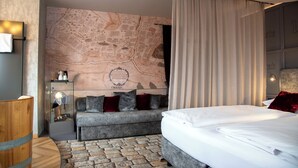Una habitación de hotel moderna con un mapa grande en la pared, un sofá gris, una mesita de madera y una cama bien hecha.