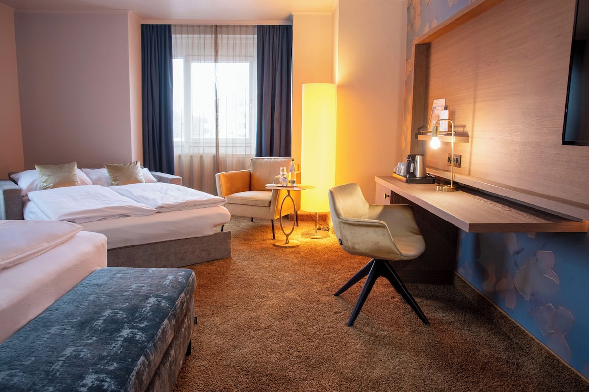 A hotel room with a bed, a desk, a chair, a lamp, and a TV.