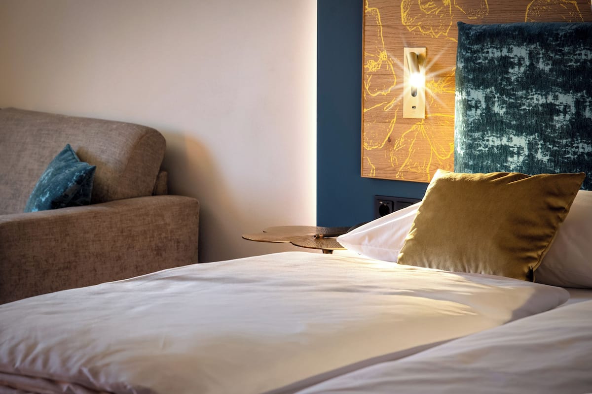 A hotel room with a bed, a sofa, and a wall-mounted light fixture.