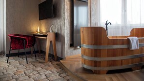 Un baño moderno con una bañera de madera, una silla roja, un escritorio de madera y un televisor montado.