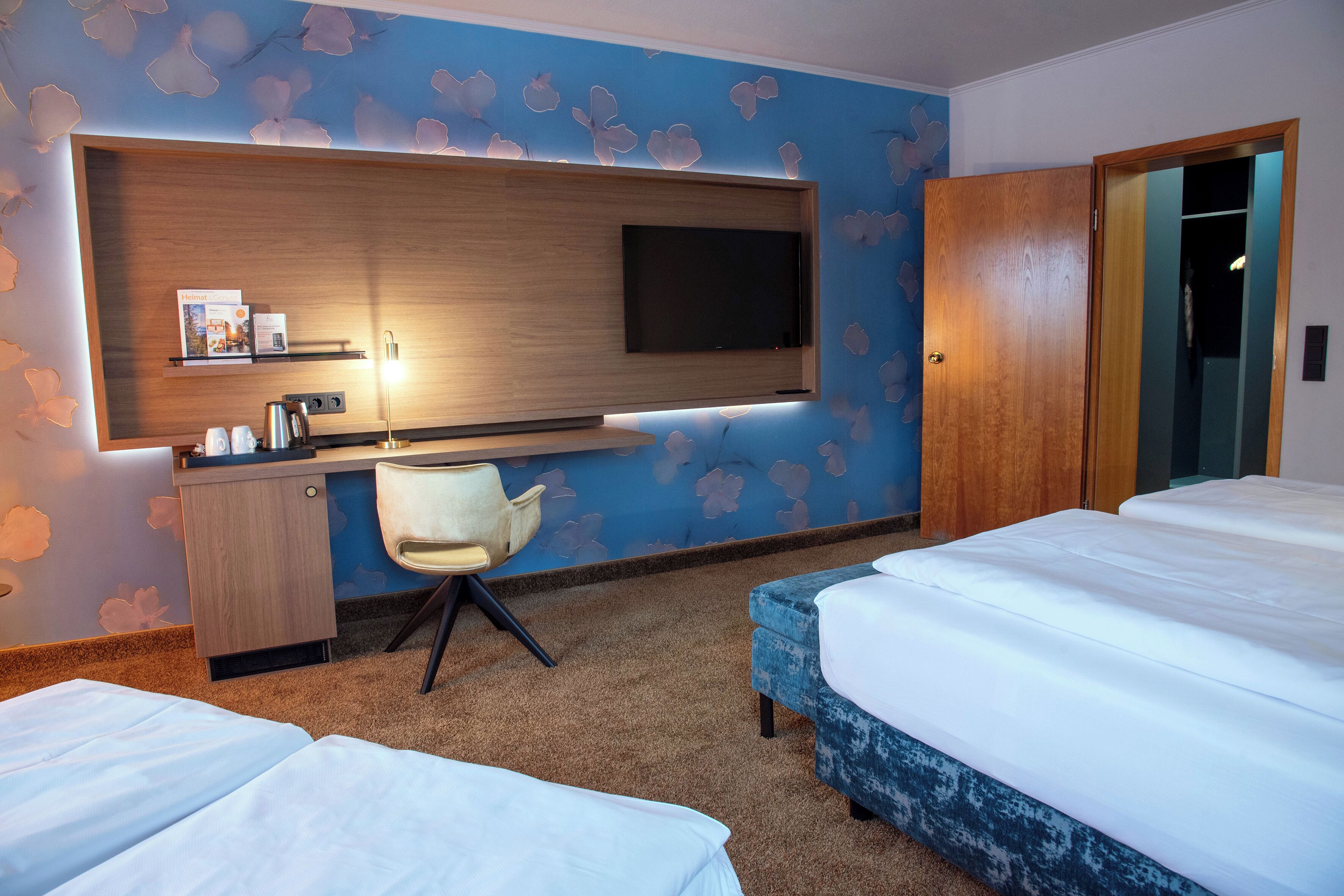 Una habitación de hotel con cama, escritorio y silla, televisión montada en la pared y armario.