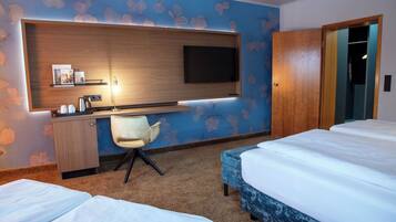 Una habitación de hotel con cama, escritorio y silla, televisión montada en la pared y armario.