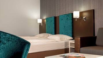 Een hotelkamer met een bed, twee stoelen, een kleine tafel en een wandlamp.