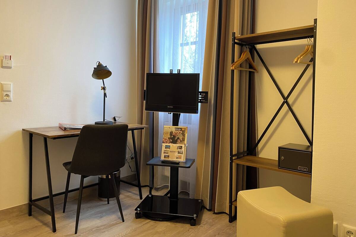 A hotel room with a desk, chair, TV, and a small table with a brochure.