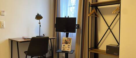 Habitación de hotel con escritorio, silla, televisión y una mesita con un folleto.
