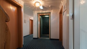 A hallway with a patterned carpet, wooden doors, and a ceiling light fixture. - AKZENT Hotel Schranne (Rothenburg ob der Tauber)