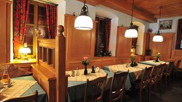 A dining area with wooden tables and chairs, hanging lamps, and floral centerpieces.