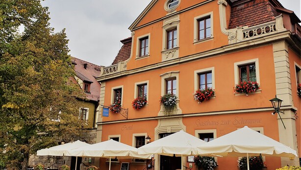 A hotel with outdoor seating under umbrellas, a stone facade, and flower boxes on the windows. - AKZENT Hotel Schranne (Rothenburg ob der Tauber)