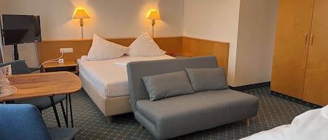A hotel room with a bed, a sofa, a table, and a TV.