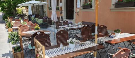 An outdoor café with wooden tables and chairs, umbrellas, and potted plants.