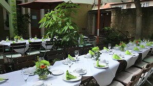 An outdoor dining area with tables set for a meal, surrounded by greenery and a building in the background. - AKZENT Hotel Schranne (Rothenburg ob der Tauber)