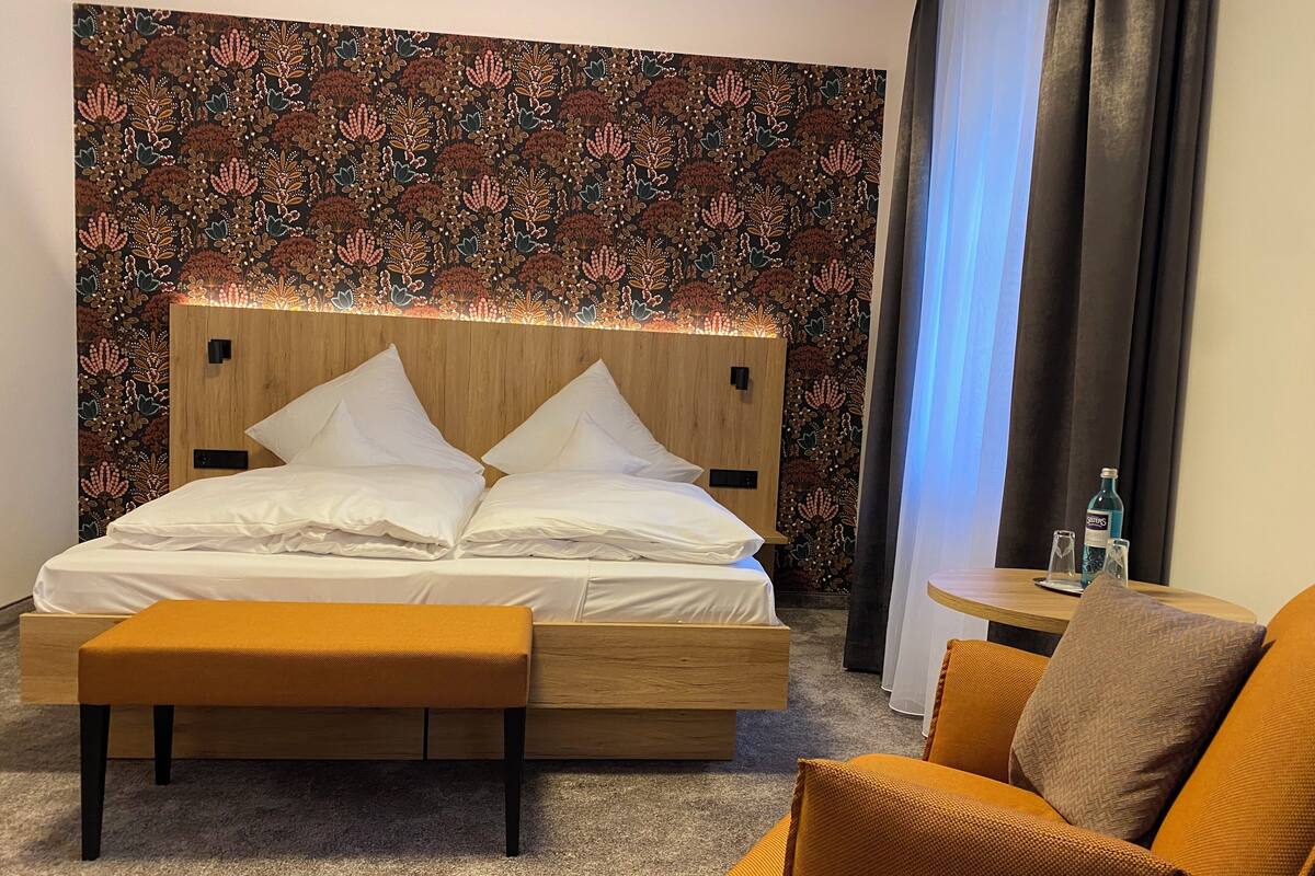 A neatly arranged hotel room with a bed, a small table, a chair, and a decorative wall.