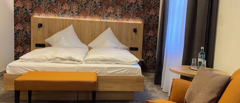 Habitación de hotel ordenada con una cama, una mesita, una silla y un adorno en la pared.