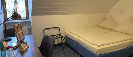 Quarto pequeno e bem arrumado, com uma cama de solteiro, escrivaninha com cadeira, radiador e janela com cortinas.