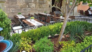 An outdoor café with tables and chairs, surrounded by greenery and a stone building. - AKZENT Hotel Schranne (Rothenburg ob der Tauber)