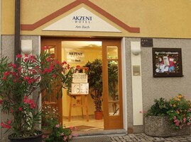Exterior del AKZENT HOTEL Am Bach, con una entrada despejada, plantas en macetas y un cartel.