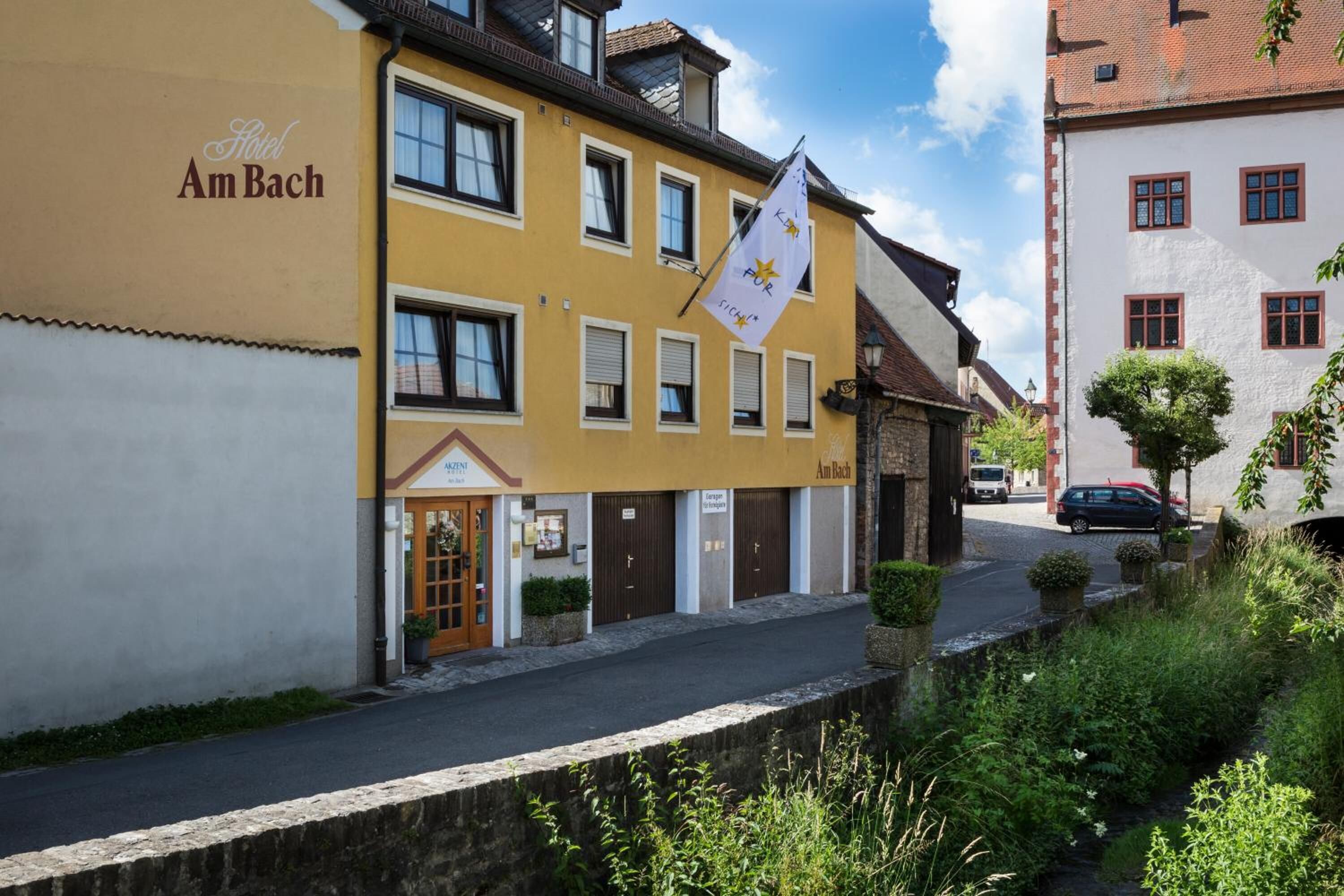 A yellow building with the sign "Hotel Am Bach" and a flag with a star and the word "SICH".
