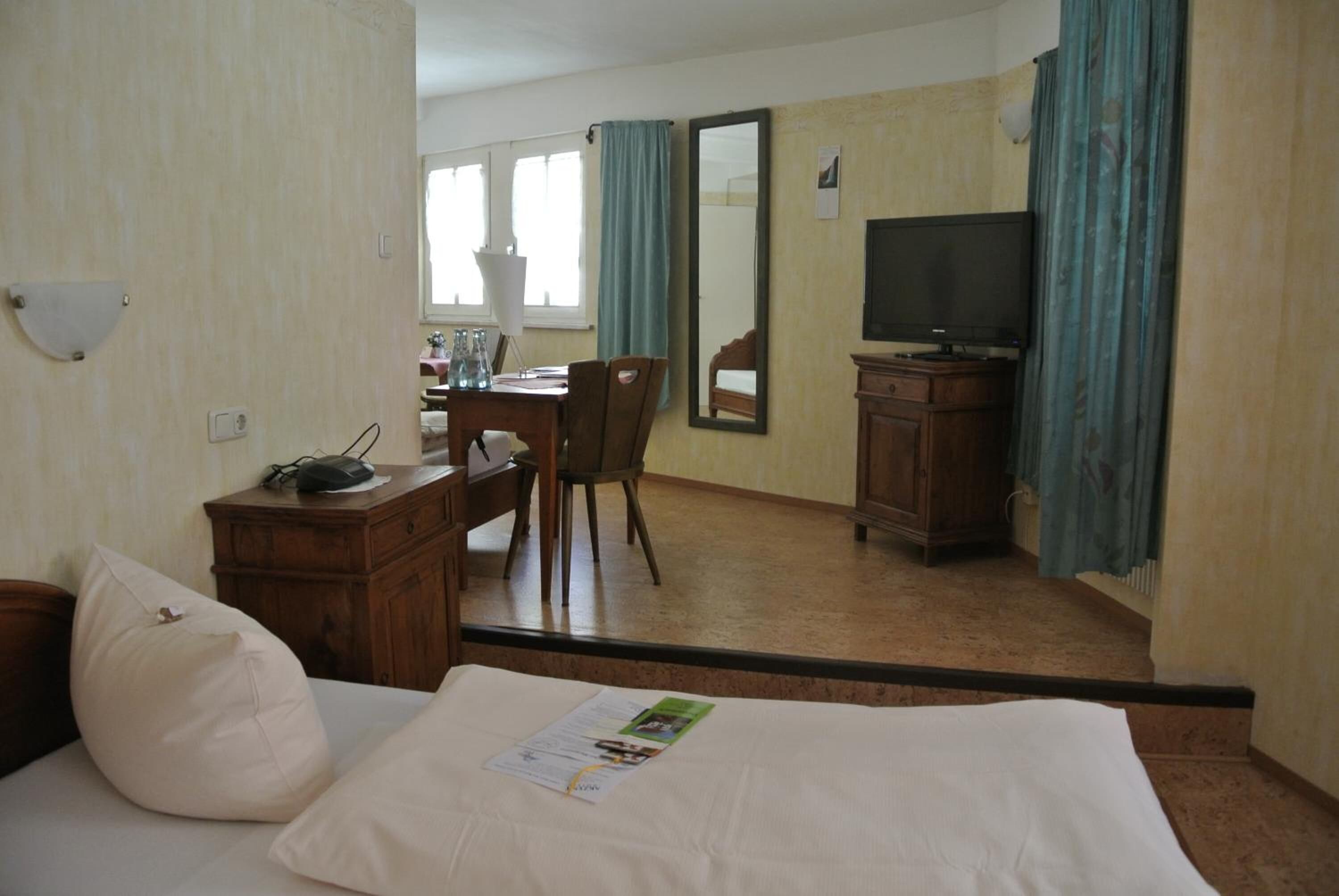 A hotel room with a bed, a desk, a chair, a television, and a mirror.