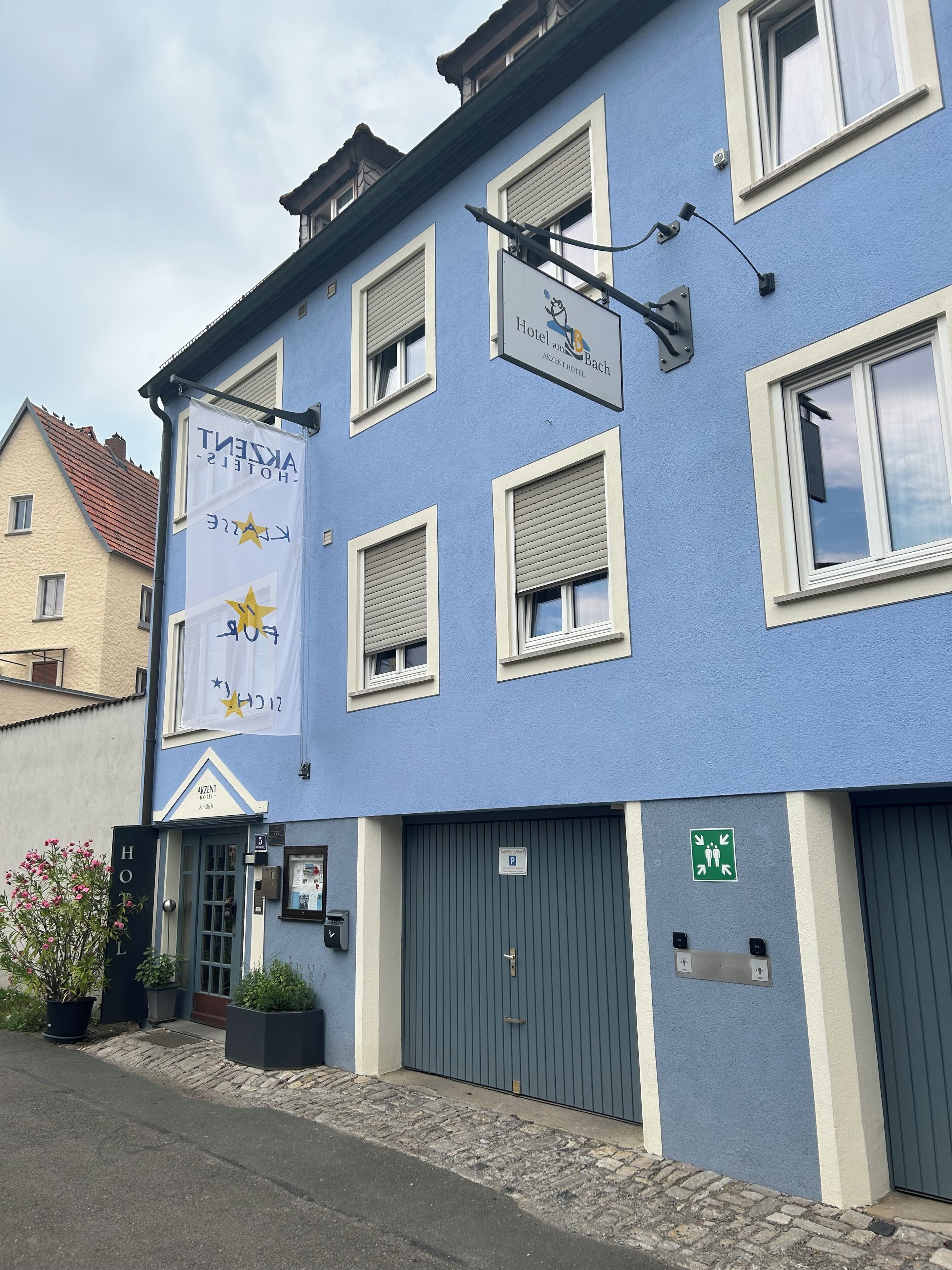 A hotel with a blue facade, multiple windows with shutters, a signboard, and a parking sign.