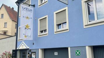 Un hotel con fachada azul, varias ventanas con contraventanas, un letrero y una señal de estacionamiento.