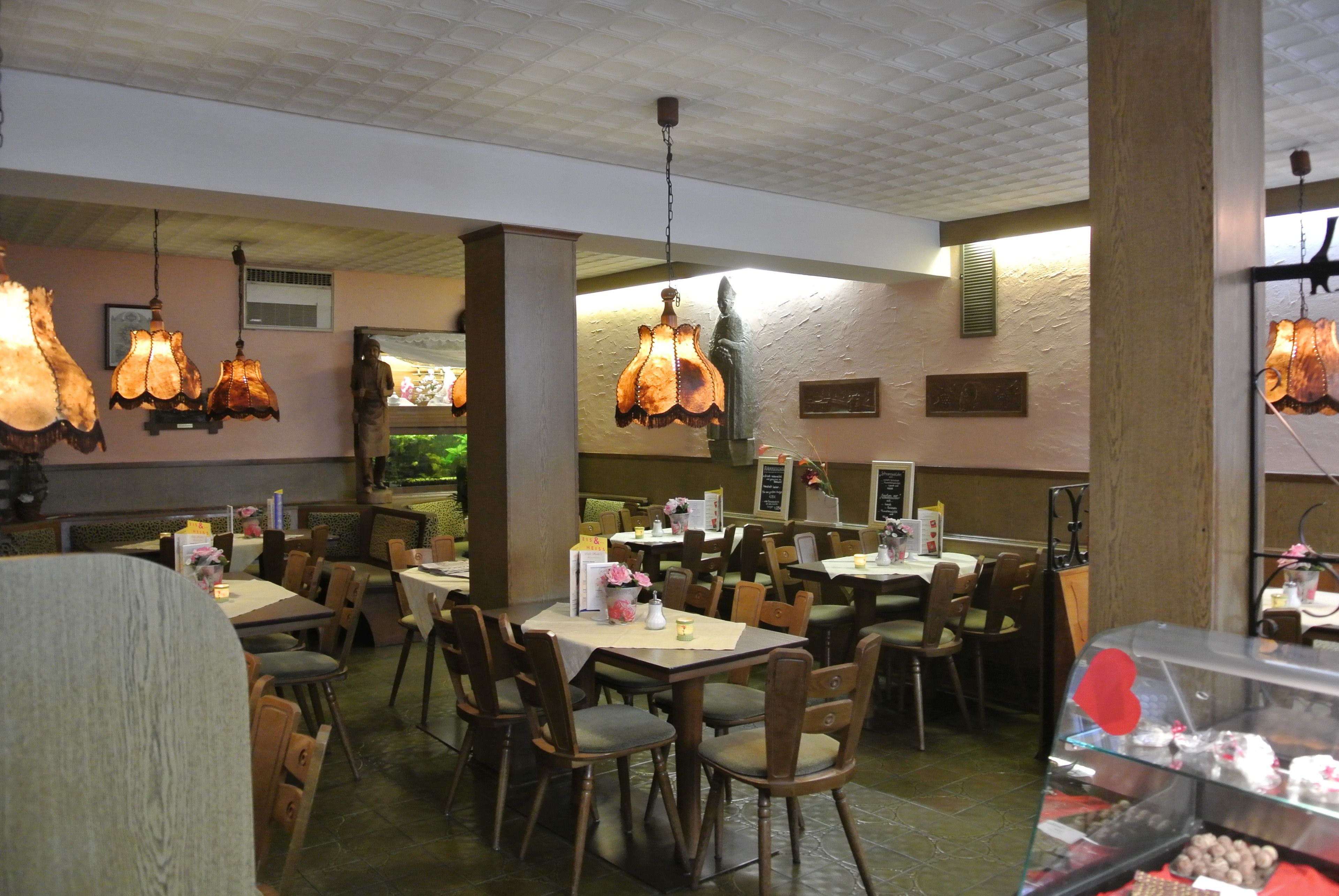 Interior de restaurante con varias mesas y sillas, lámparas colgantes y una vitrina con postres.