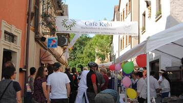 Escena callejera con un café llamado Café Kehl, que presenta un banderín y una carpa con globos.