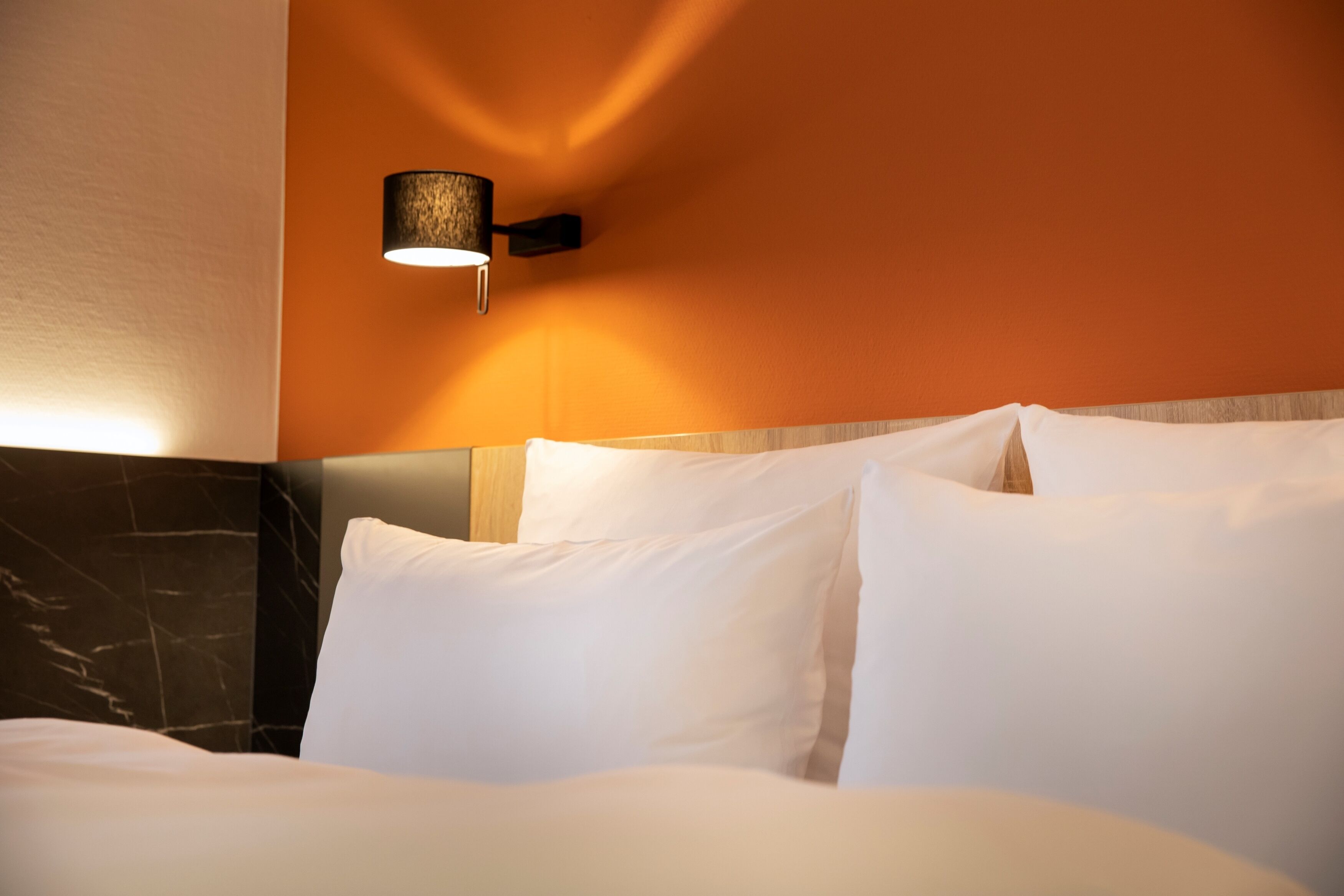 Una habitació d'hotel amb llit, almoines blanques, un reposacapses de marbre i una làmpada penjada a la paret.