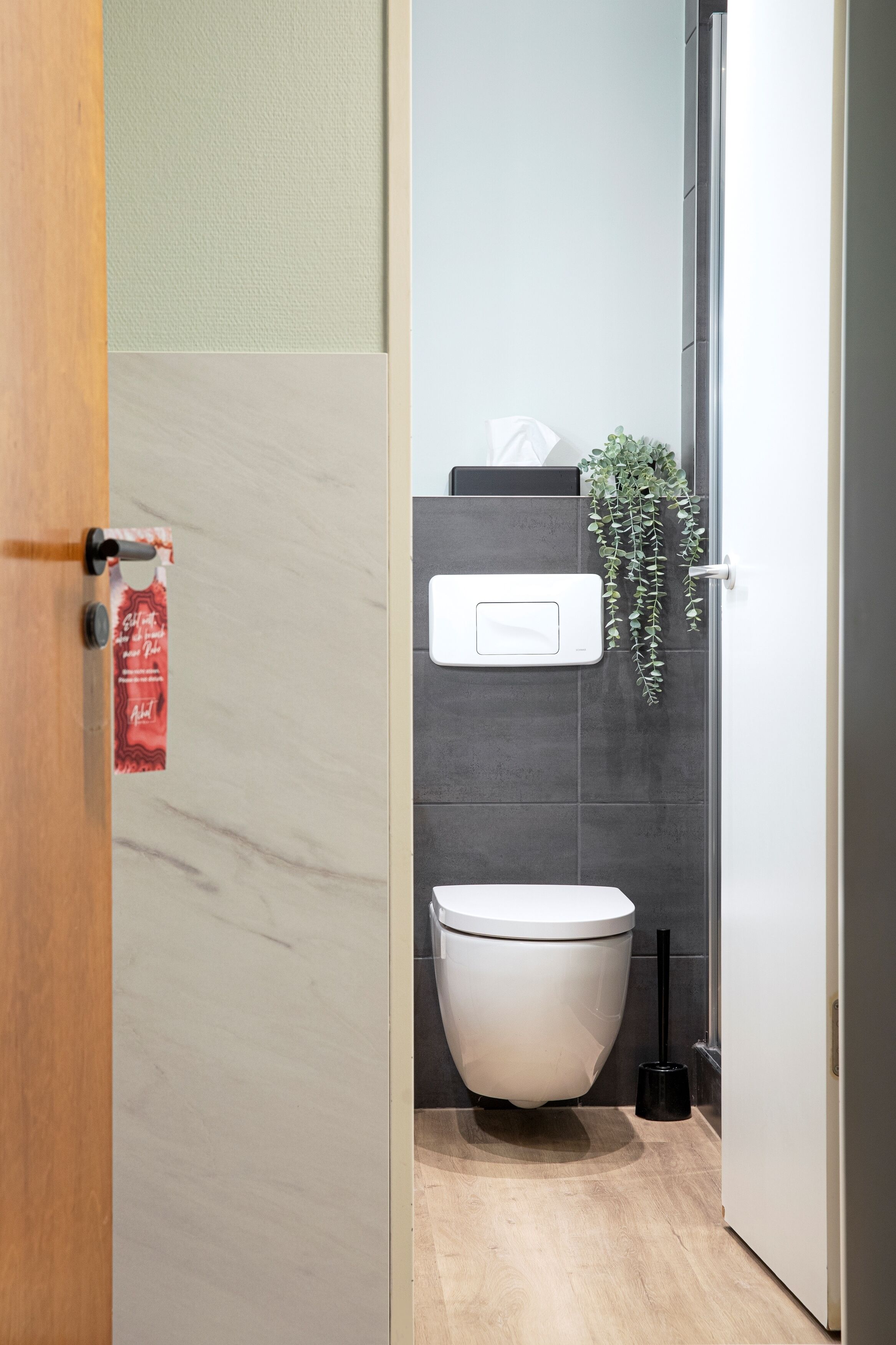 A modern bathroom with a toilet, a hand dryer, and a small plant.