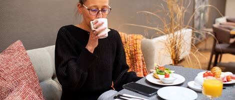 A person sitting at a table with breakfast items, a smartphone, and a glass of orange juice.